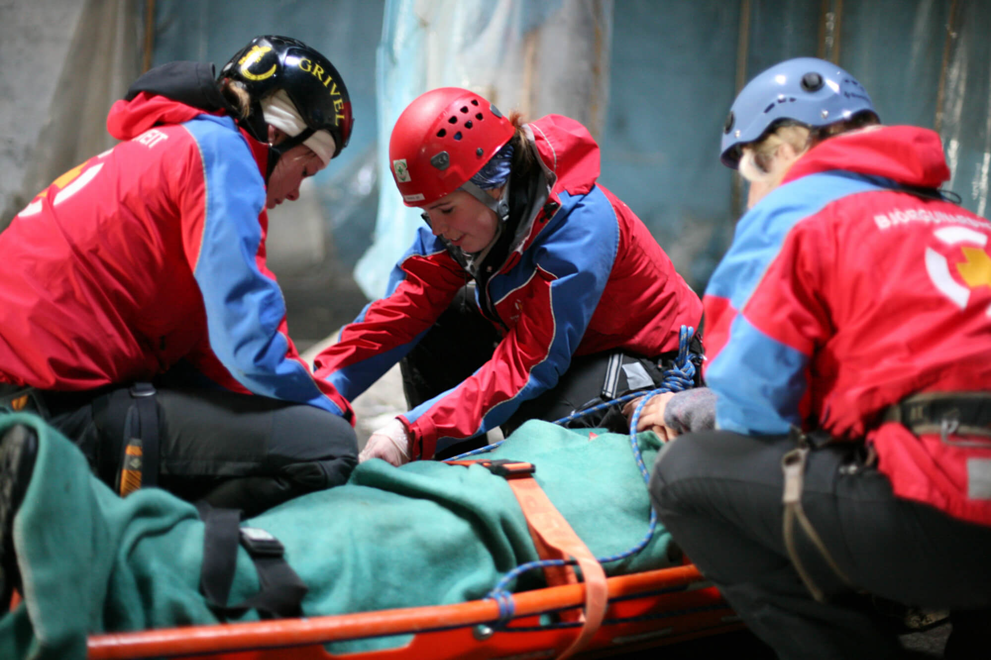 Rescue team in red and blue jackets assisting an injured person on a stretcher during a mountain rescue operation.